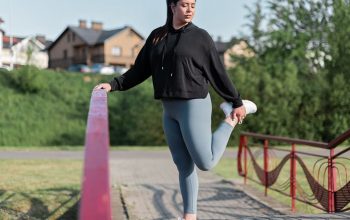 Young woman in activewear stretching on a red railing outdoors.
